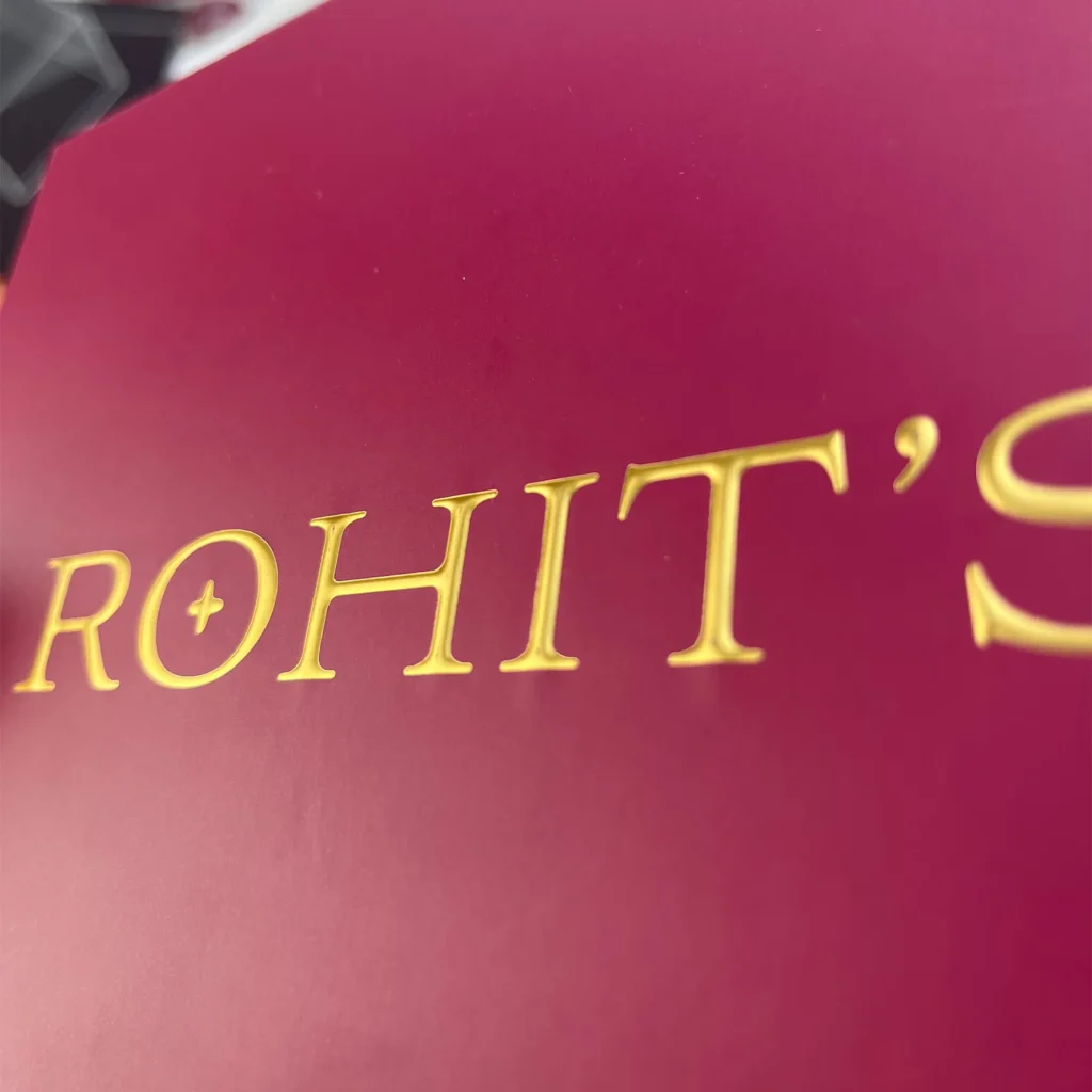 Close-up of gold hot foil stamping combined with embossing on a matte burgundy rigid box, showing 3D raised texture and sharp metallic edges.