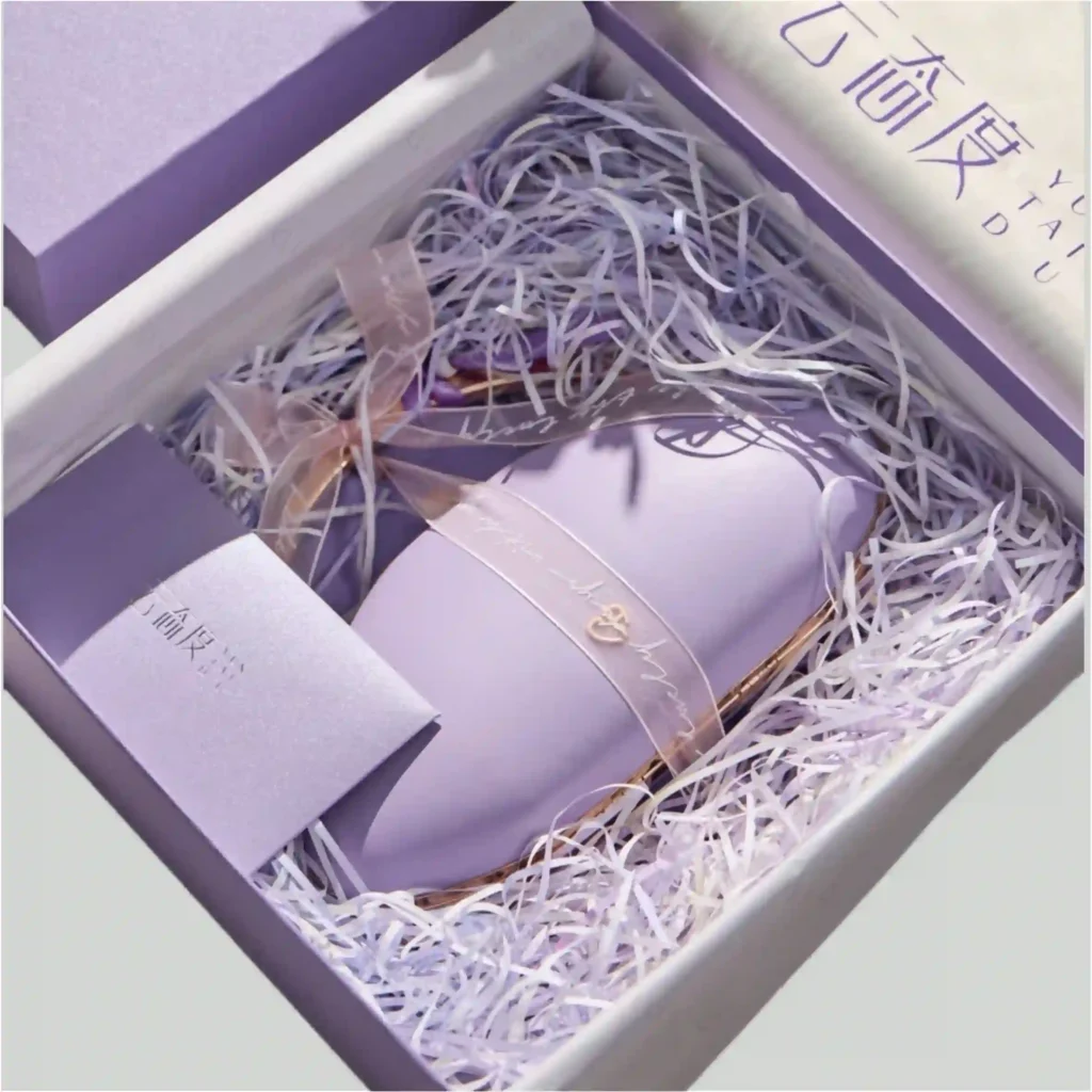 Luxury purple gift box filled with white crinkle paper shreds (raffia). Flexible void fill holding a beauty device and card without a custom mold.