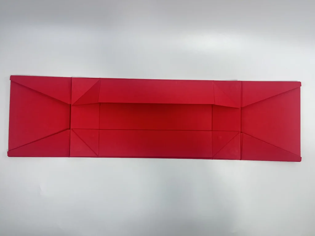 Red double door folding magnetic box laid flat showing wide panel structure with corner gussets for space-saving bulk shipping of luxury rigid packaging
