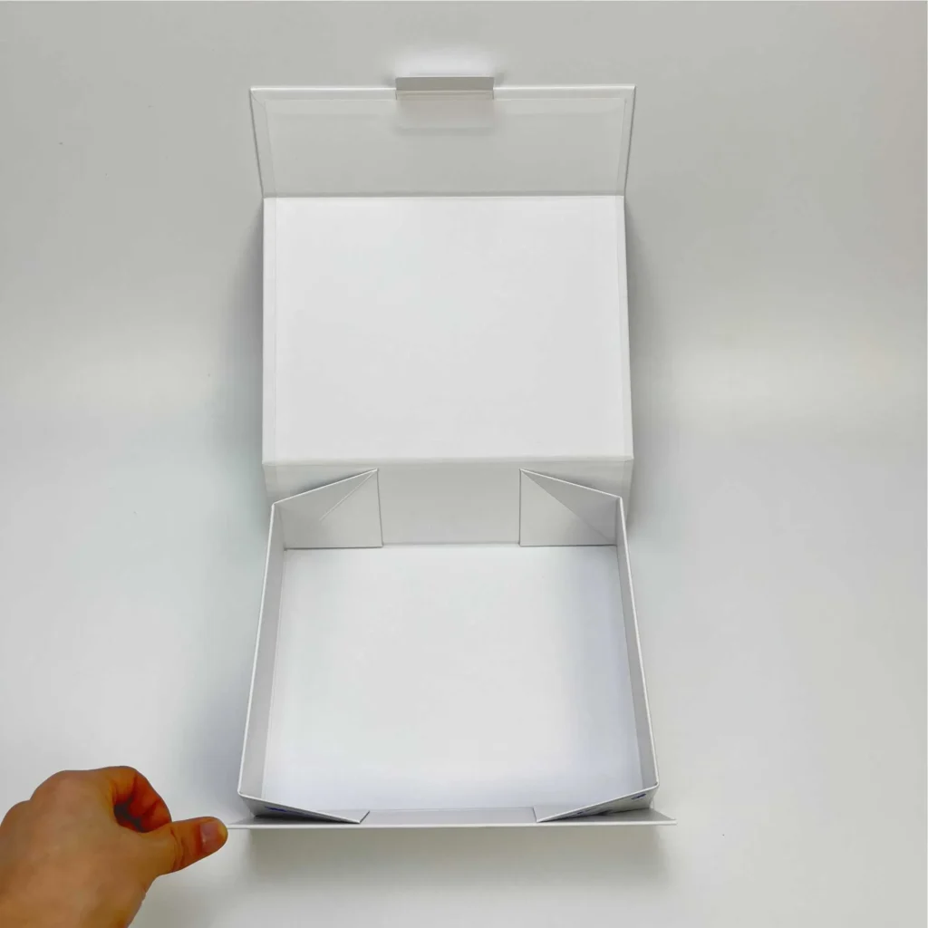 White collapsible rigid box with paper tab open from above showing clean interior snap corner gusset structure and lid detail