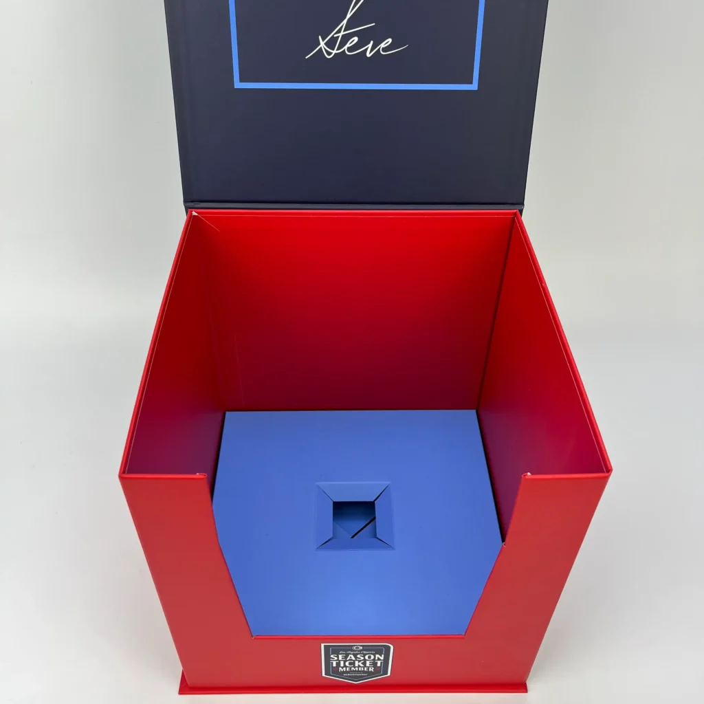 Interior view of open side-folding collapsible rigid cube box showing red inner walls custom printed lid and blue snap-lock base insert for luxury gift packaging